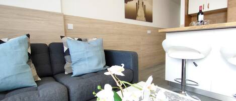 A modern living room with a grey sofa, blue cushions, and a white orchid vase.