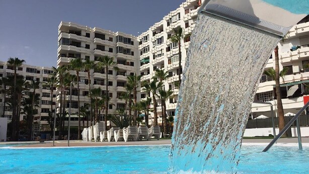 Una piscina con fuente, rodeada de palmeras y edificios de varios pisos.