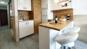 Una cocina moderna con armarios blancos, un muro decorativo de madera, un horno empotrado y una cafetera sobre la encimera.