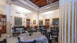 Un comedor amplio con varias mesas y sillas, columnas ornamentadas y candelabros.
