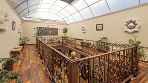 Un amplio atrio con techo alto y cúpula de cristal, que cuenta con suelo de madera, barandillas de metal ornamentadas y numerosas plantas en macetas.