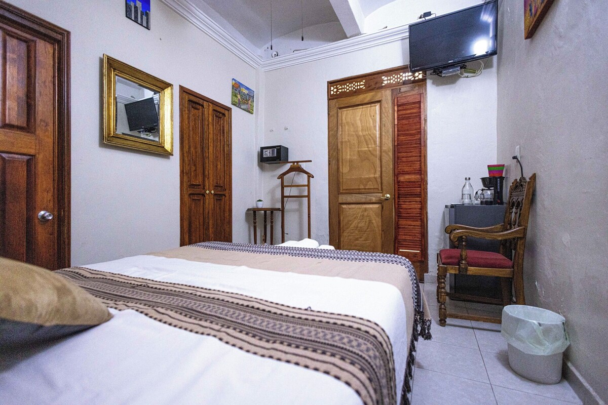 Un dormitorio con cama, armario de madera, televisor y una pequeña mesa.
