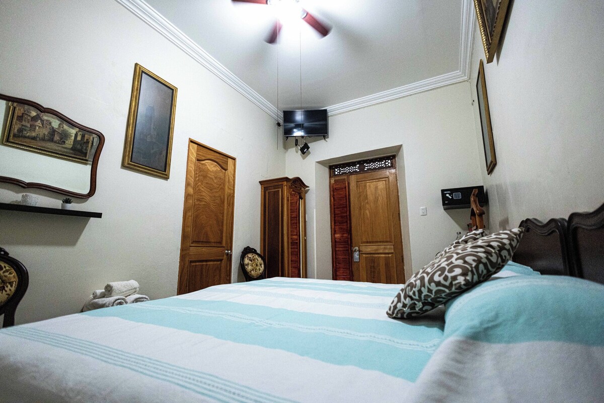 Un dormitorio con cama, ventilador de techo, televisor, puertas de madera y espejo.