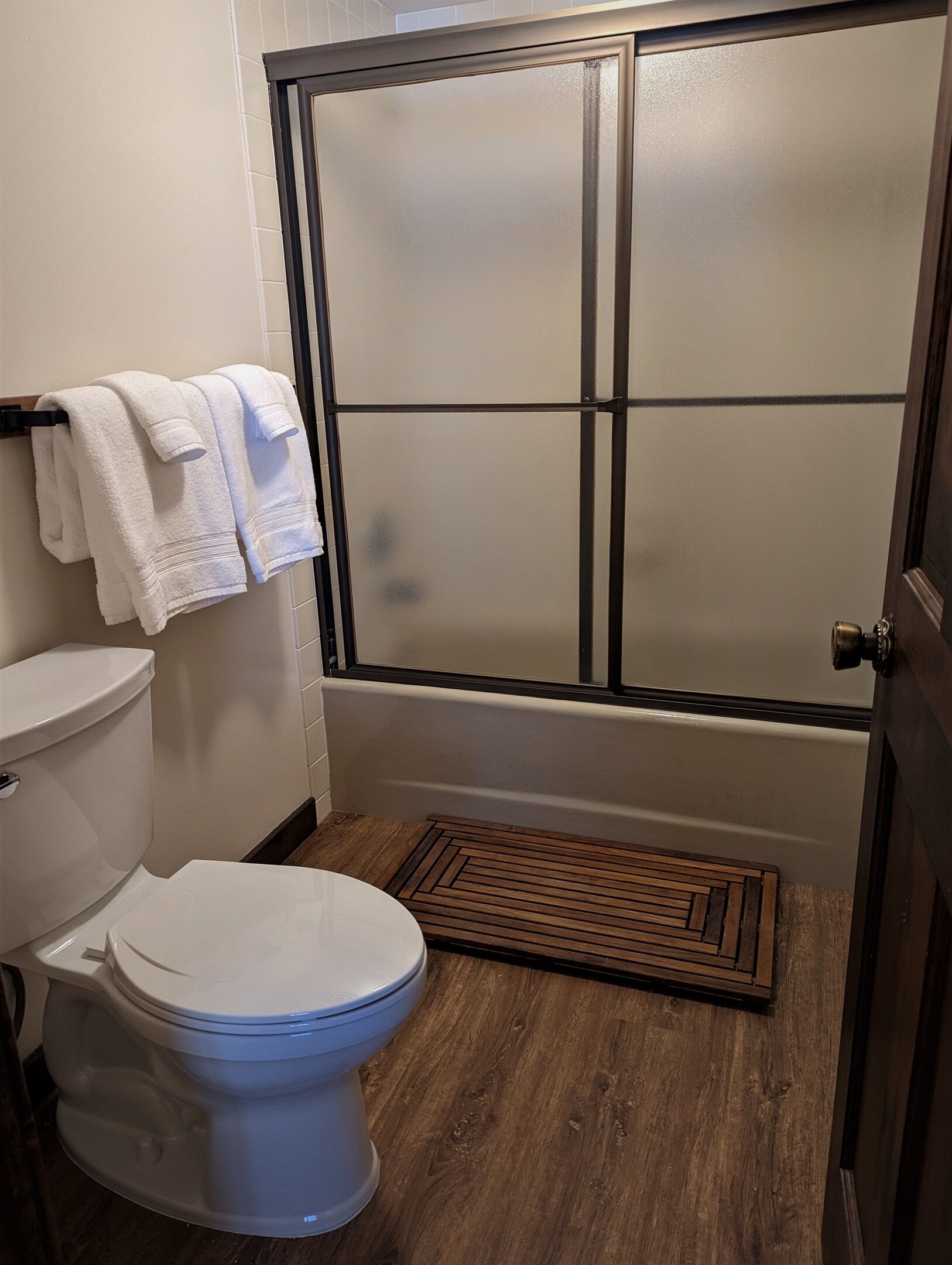 Ein Badezimmer mit Toilette, Duschkabine und Holzbadezimmerteppich.