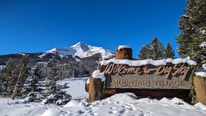 Cartello di benvenuto innevato per Mountain Village, con una montagna sullo sfondo.