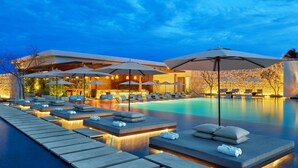Un área junto a la piscina con sillones de descanso y sombrillas, piscina y un edificio de diseño moderno.