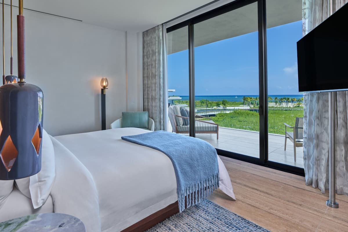 A modern hotel room with a large bed, a TV, and a balcony with a view of the ocean.