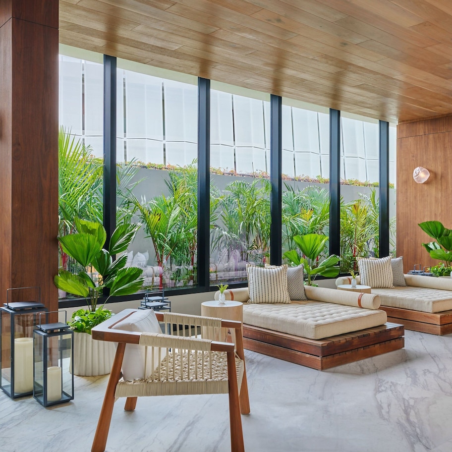 A modern living room with a sofa set, a rattan chair, and a hanging chair. Large windows provide a view of greenery outside.