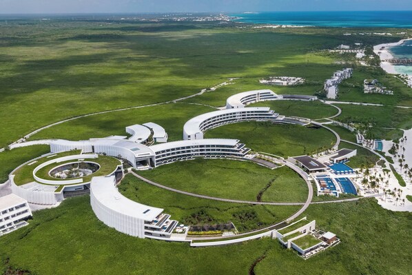 An aerial view of a modern resort with a central circular building, surrounded by lush greenery and a beach. - The St. Regis Kanai Resort, Riviera Maya (Playa del Carmen)