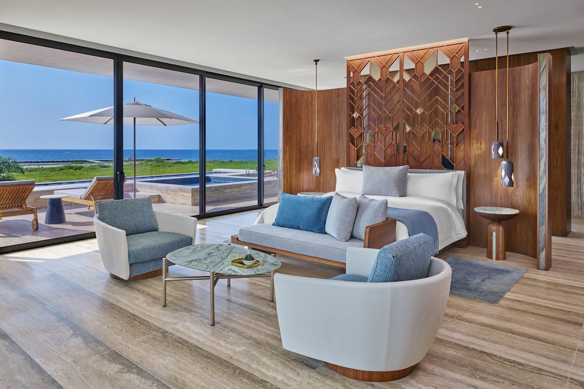 A modern living room with a large window overlooking a pool and the ocean. There is a sofa, a coffee table, and a side table.