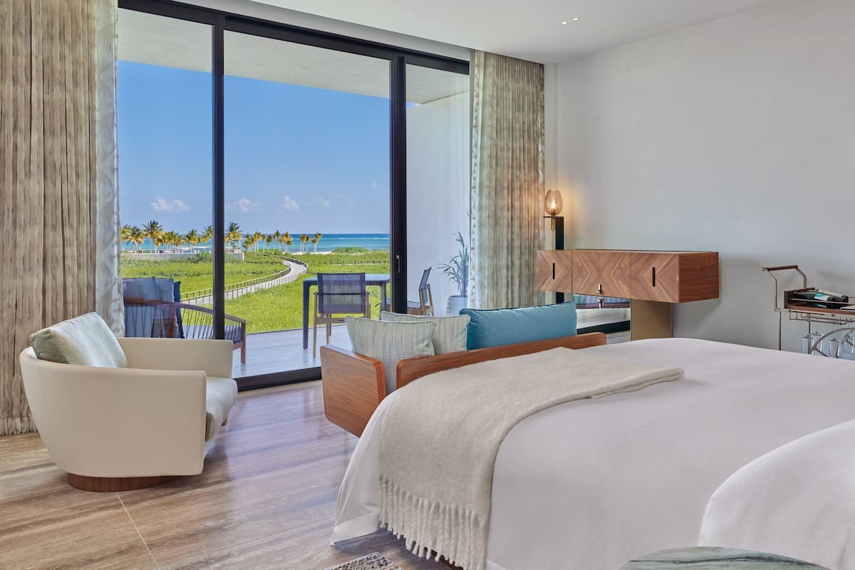 A modern hotel room with a large bed, a seating area with a view of the beach, and a wooden cabinet.