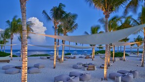 A beach setting with palm trees, beach chairs, and lounge areas.