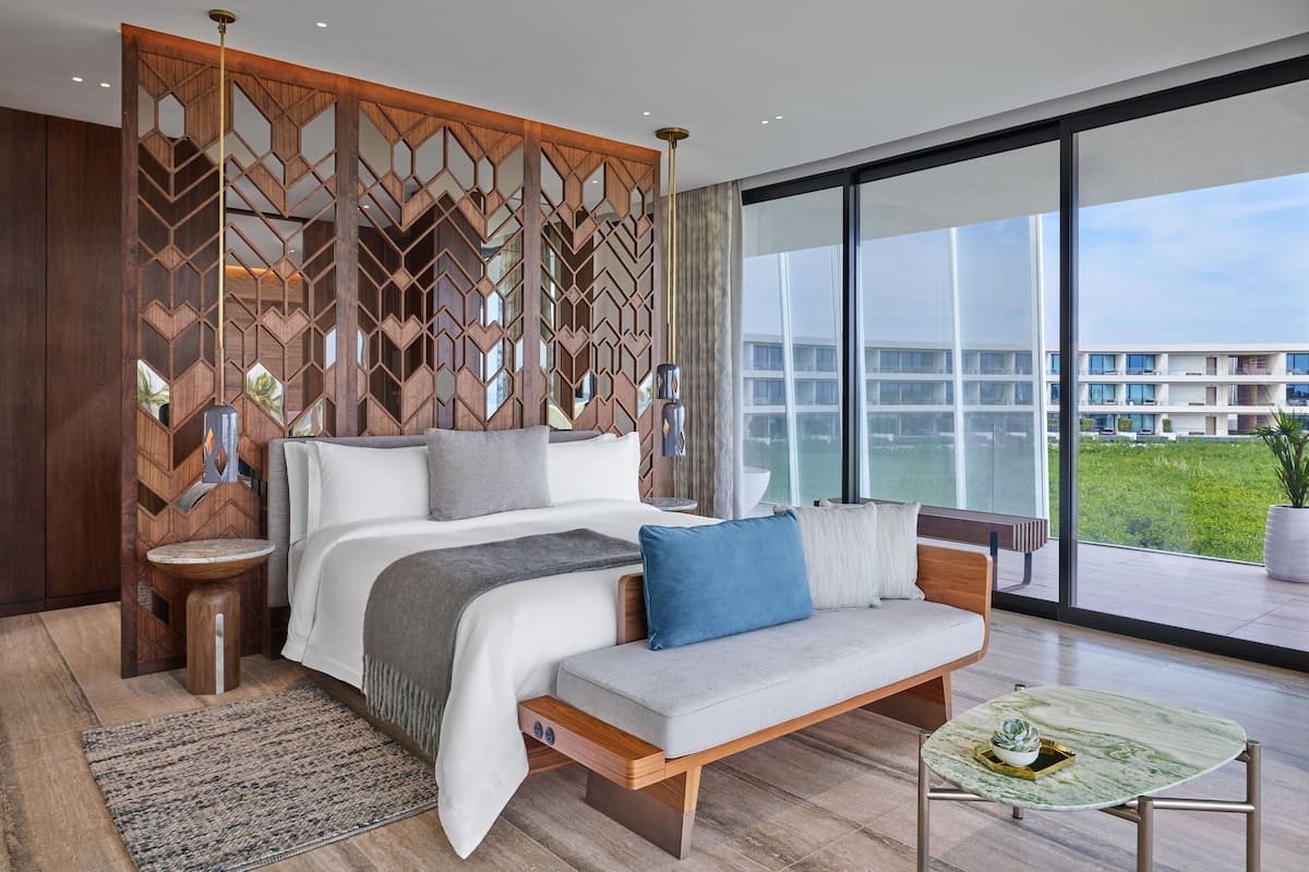 A modern bedroom with a large bed, a sofa, a small table, and a view of a building through large windows.
