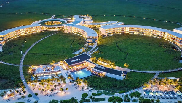 A large resort with multiple circular buildings, a central pool, and a beach area with sun loungers.