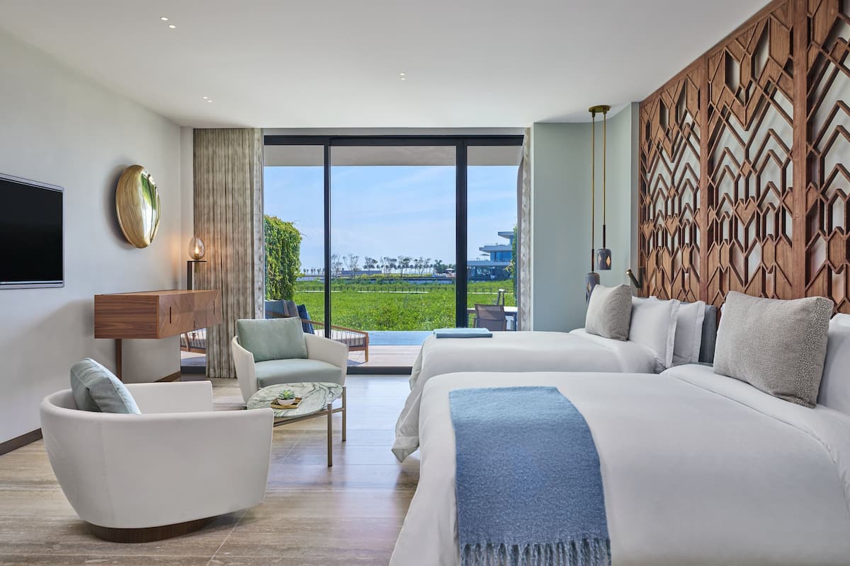 A modern hotel room with a large bed, a sofa, a TV, and a view of the outdoors.