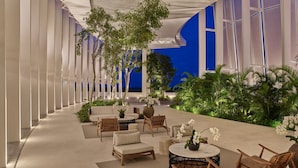 A modern indoor garden with seating areas, potted plants, and a view of the night sky.