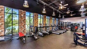 A gym with exercise equipment, large windows, and a brick wall.
