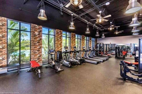 Ein Fitnessstudio mit Trainingsgeräten, großen Fenstern und einer Ziegelwand.