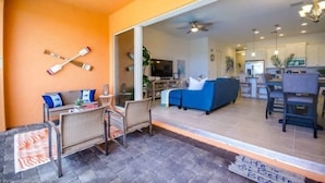An open-plan living area with a blue sofa, wicker furniture, and a kitchen in the background.