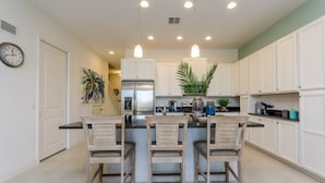 A kitchen with white cabinets, a central island with three chairs, a refrigerator, and pendant lighting.