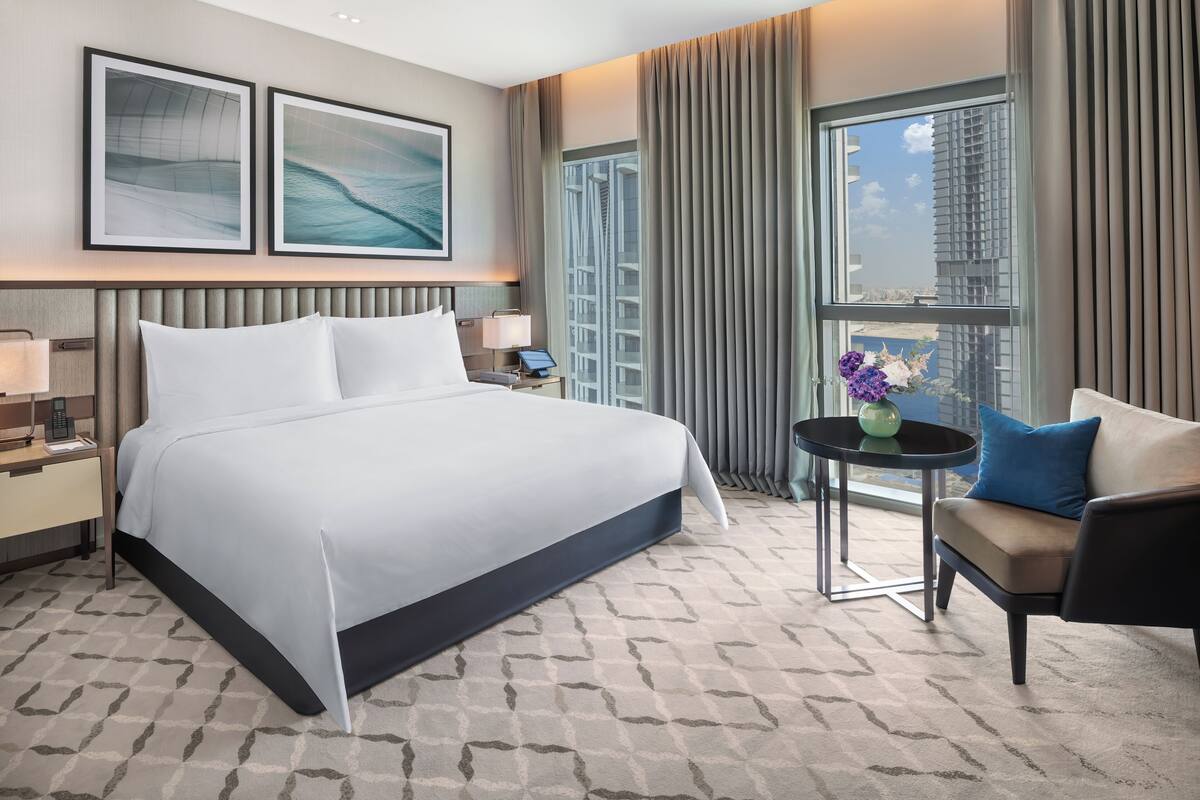 Habitación de hotel con una cama grande, un escritorio, una silla y vistas a la ciudad.
