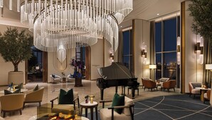 Un vestíbulo amplio con un piano de cola, candelabros elegantes, asientos cómodos y ventanas grandes que ofrecen vistas a la ciudad.