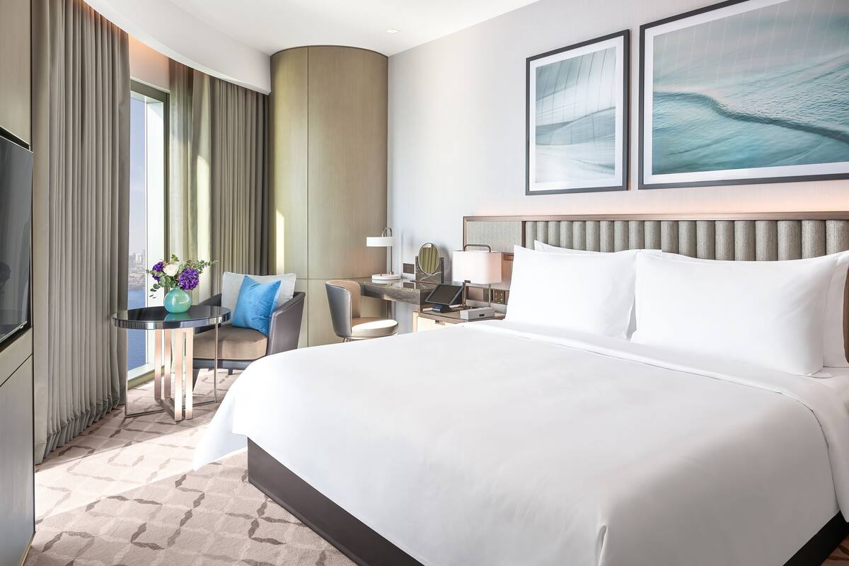 Una habitación de hotel con una cama grande, un escritorio con una computadora portátil, una silla y un televisor.