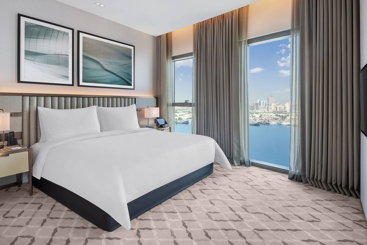 Habitación de hotel moderna con una cama grande, vista a la ciudad y paisaje urbano a través de la ventana.