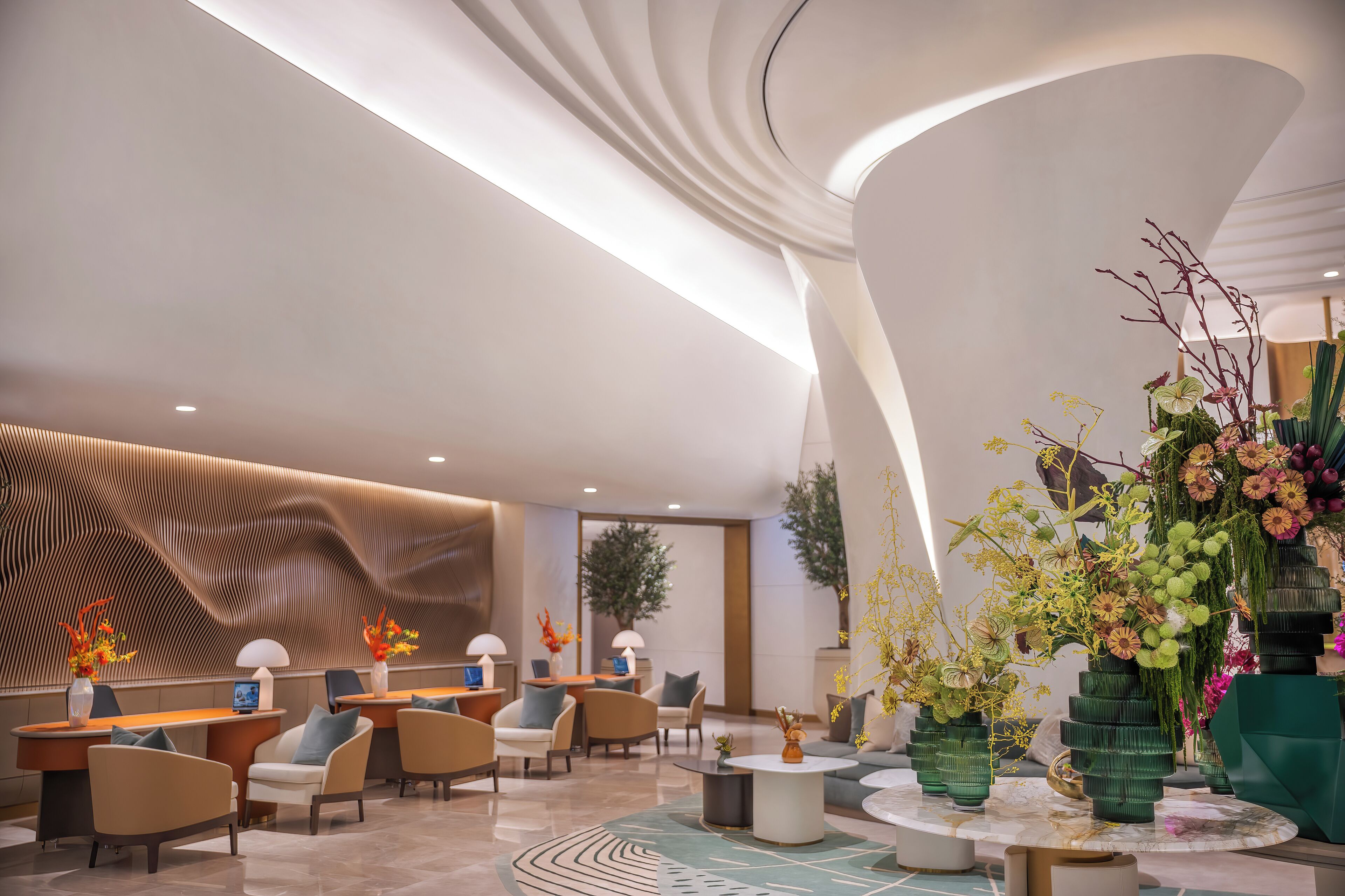 A modern lobby with curved ceiling, seating areas, and decorative plants.