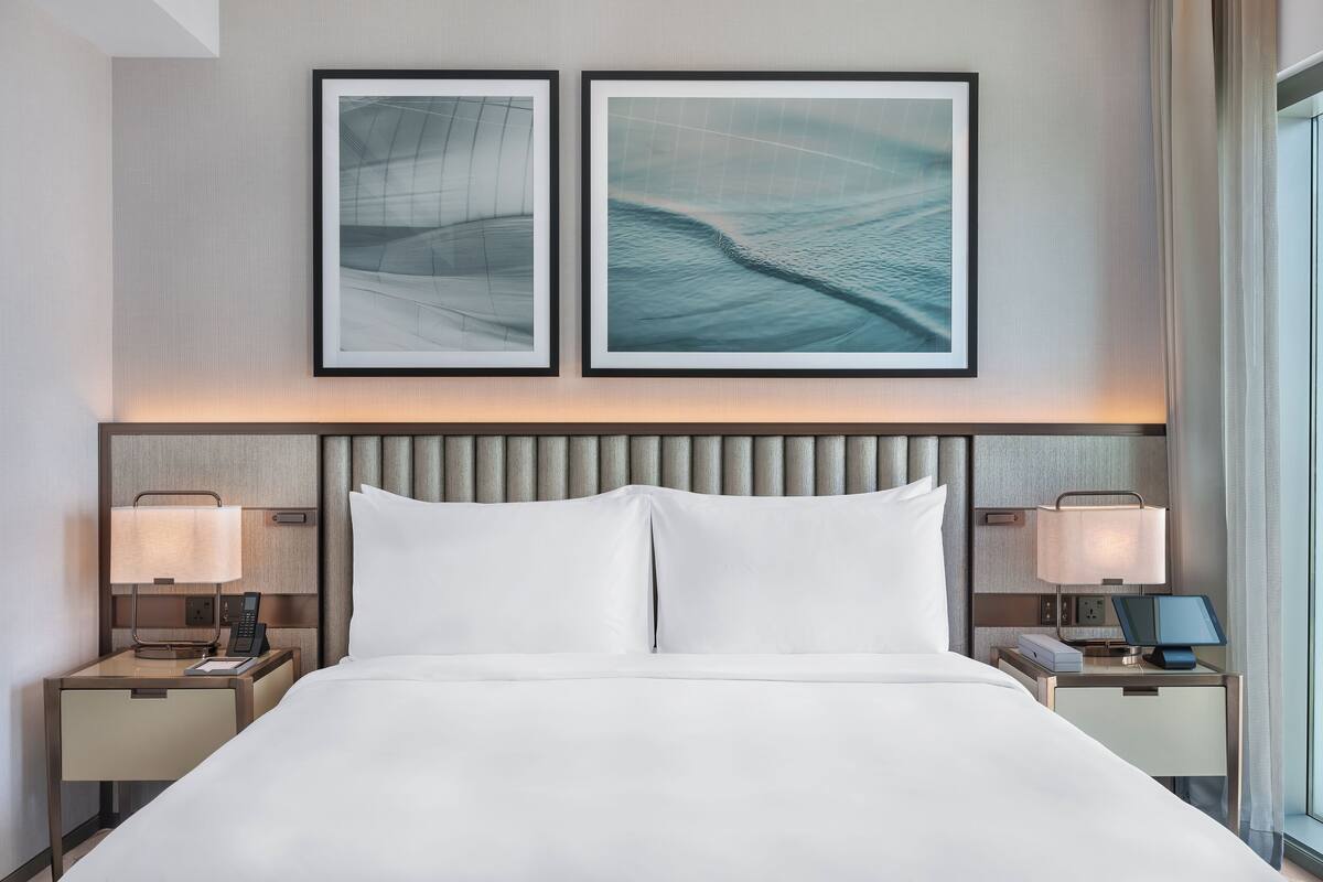 Una habitación de hotel con una cama grande, dos mesitas de noche con lámparas, un televisor de pantalla plana y dos obras de arte enmarcadas en la pared.