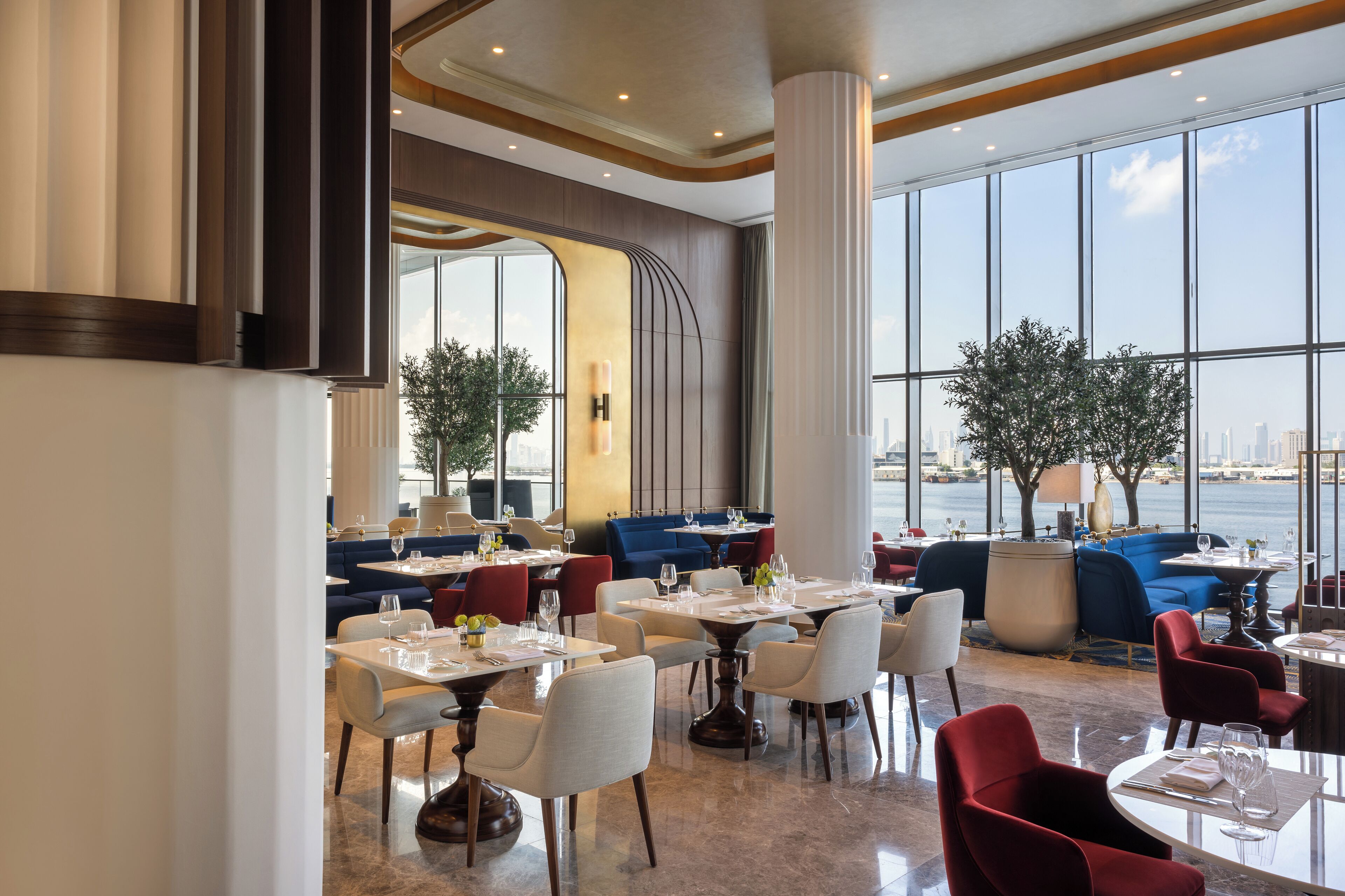 A modern restaurant with tables and chairs, large windows, and a view of the city.