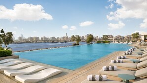 A rooftop infinity pool with lounge chairs and a city skyline in the background. - Address Creek Harbour (Dubai)