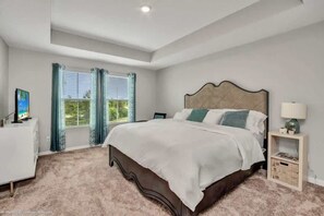 A bedroom with a large bed, a bedside table, a nightstand, and a window with curtains.