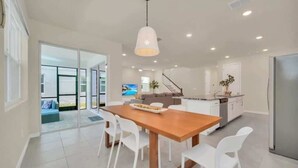 Une cuisine moderne avec une table à manger en bois, des chaises blanches et un luminaire suspendu.