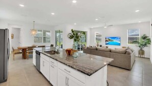Een moderne keuken met witte kasten, een marmeren aanrechtblad en een eethoek met een houten tafel en stoelen.