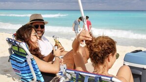 Escena de playa con gente descansando en sillas bajo un paraguas.