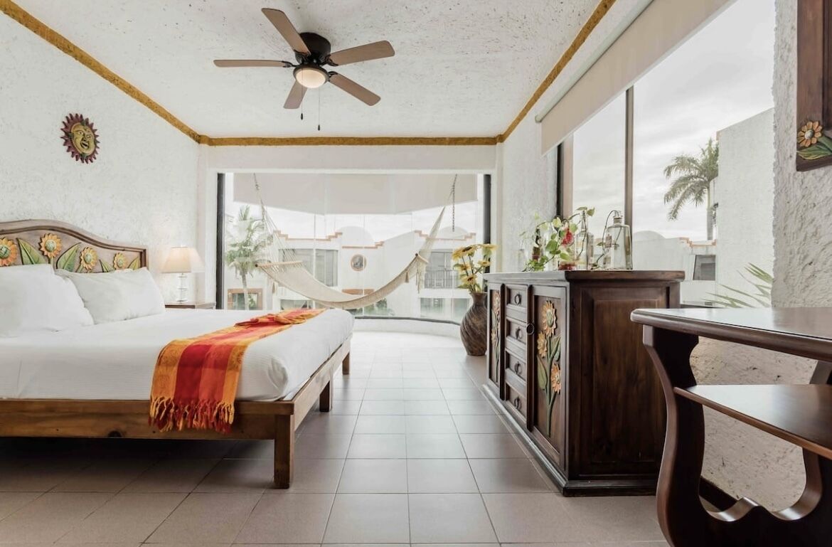 A bedroom with a bed, a ceiling fan, a large window, and a view of the outdoors.