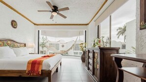 Un dormitorio con cama, ventilador de techo, ventana grande y vista al exterior.