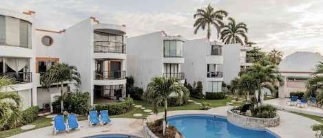 Un hôtel moderne doté d’un espace piscine, comprenant des chaises longues et des palmiers.