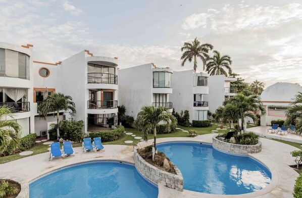 A modern hotel with a pool area, including lounge chairs and palm trees.