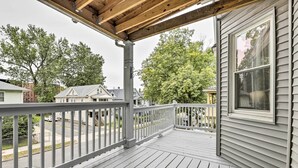 Een houten terras met een balustrade, een overdekte veranda en uitzicht op omliggende huizen en bomen.
