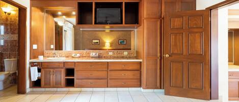 A spacious bathroom with a large vanity, a built-in television, and a wooden door.