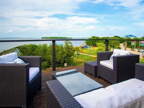 A balcony with wicker furniture and a view of the sea and greenery.
