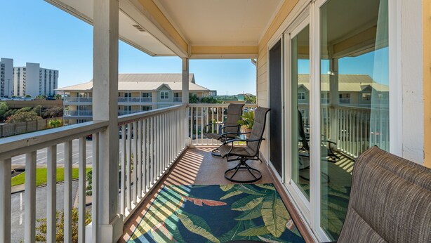 A balcony with a view of other buildings, a patterned rug, and a chair.