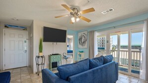 A living room with a blue sofa, a ceiling fan, a flat-screen TV, and a view of the ocean through the sliding glass doors. - 200 yards to private gated beach access! 3BR/2BA. Quiet location in Destin (Destin)