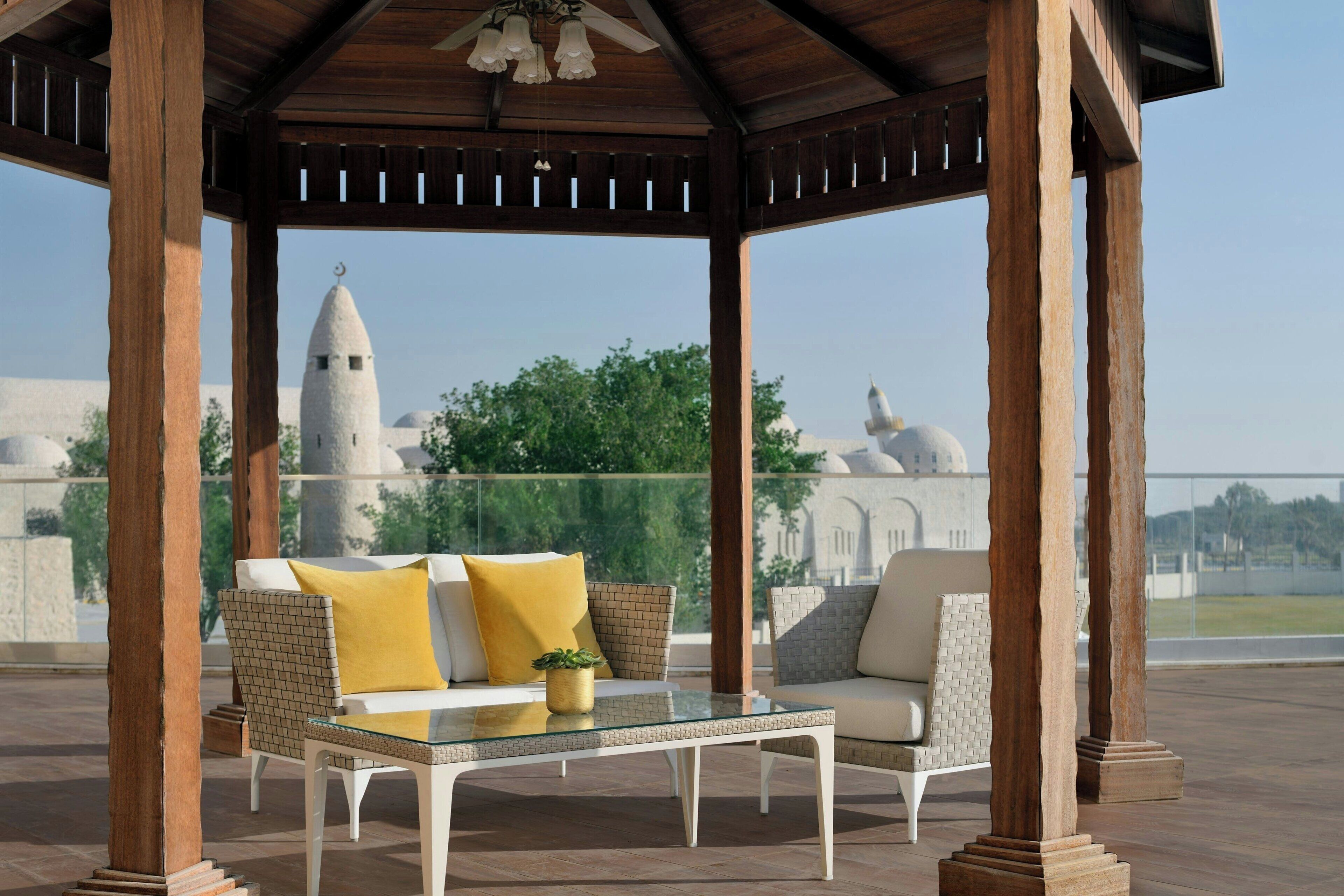 A covered outdoor seating area with a glass table and chairs, a wooden gazebo structure, and a view of a distant building with a dome.