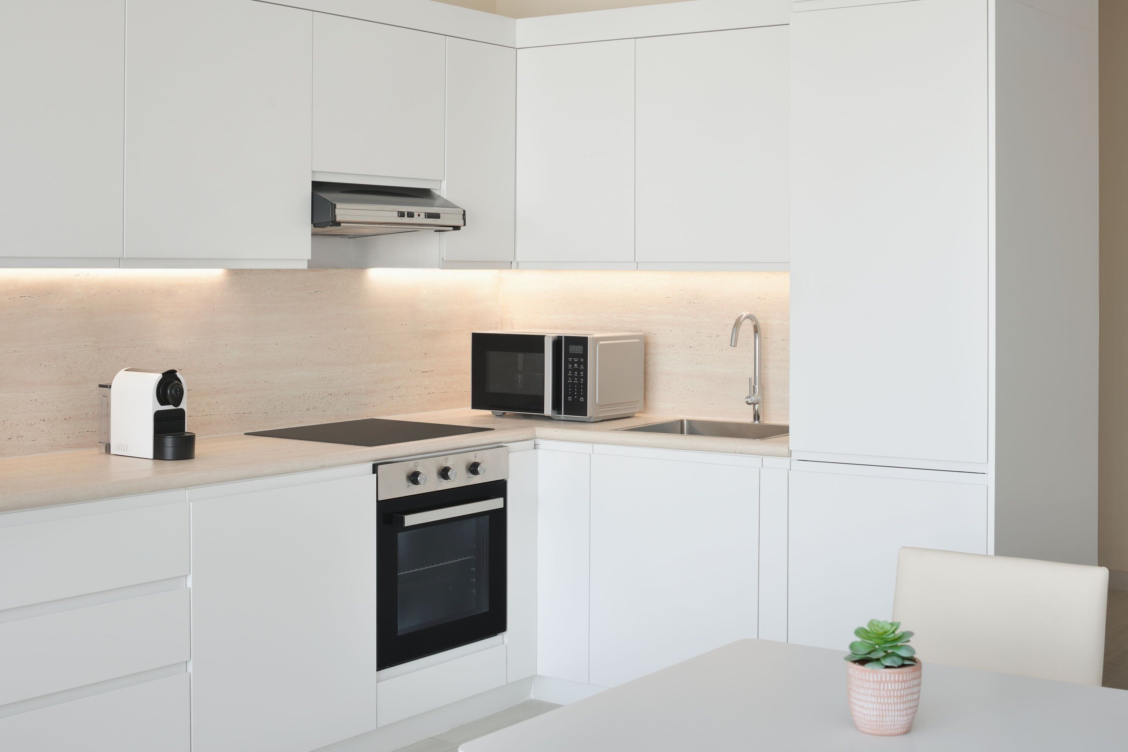 A modern kitchen with white cabinetry, a built-in microwave, a coffee maker, and a stove.