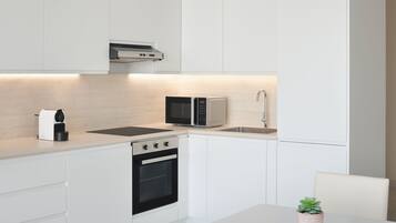 A modern kitchen with white cabinetry, a built-in microwave, a coffee maker, and a stove.