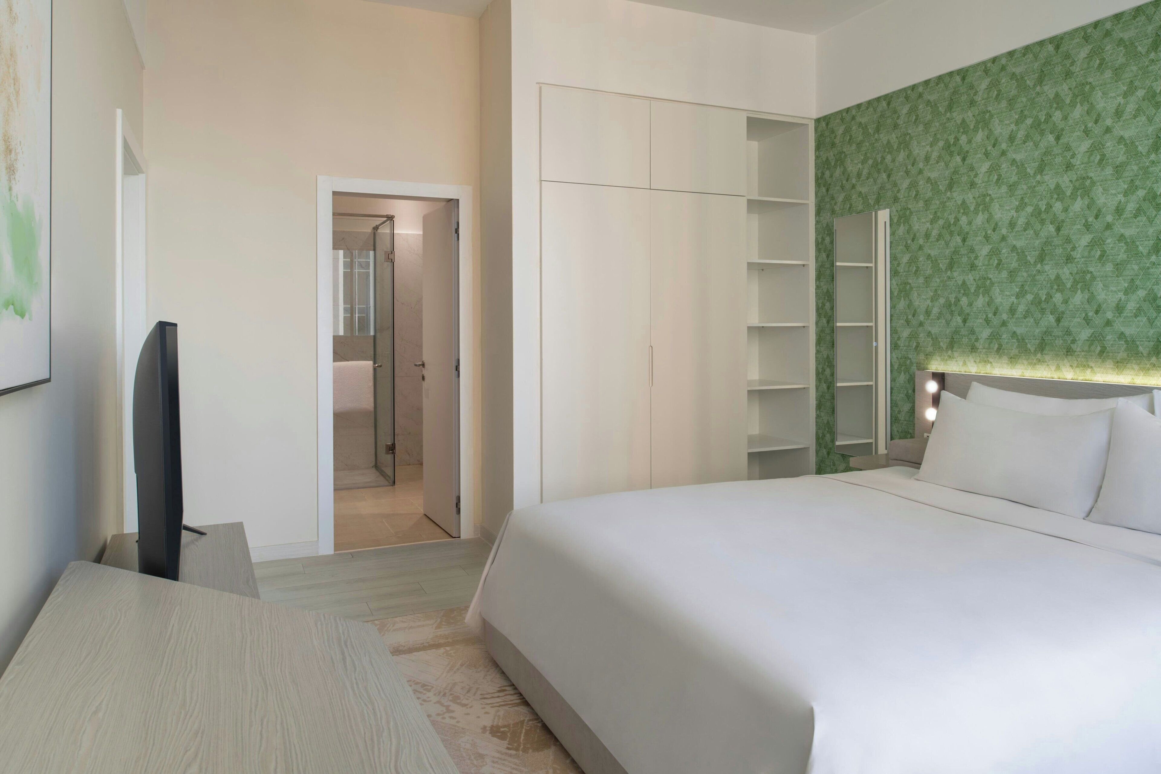 A hotel room with a bed, a television, a wardrobe, and a green patterned wall.