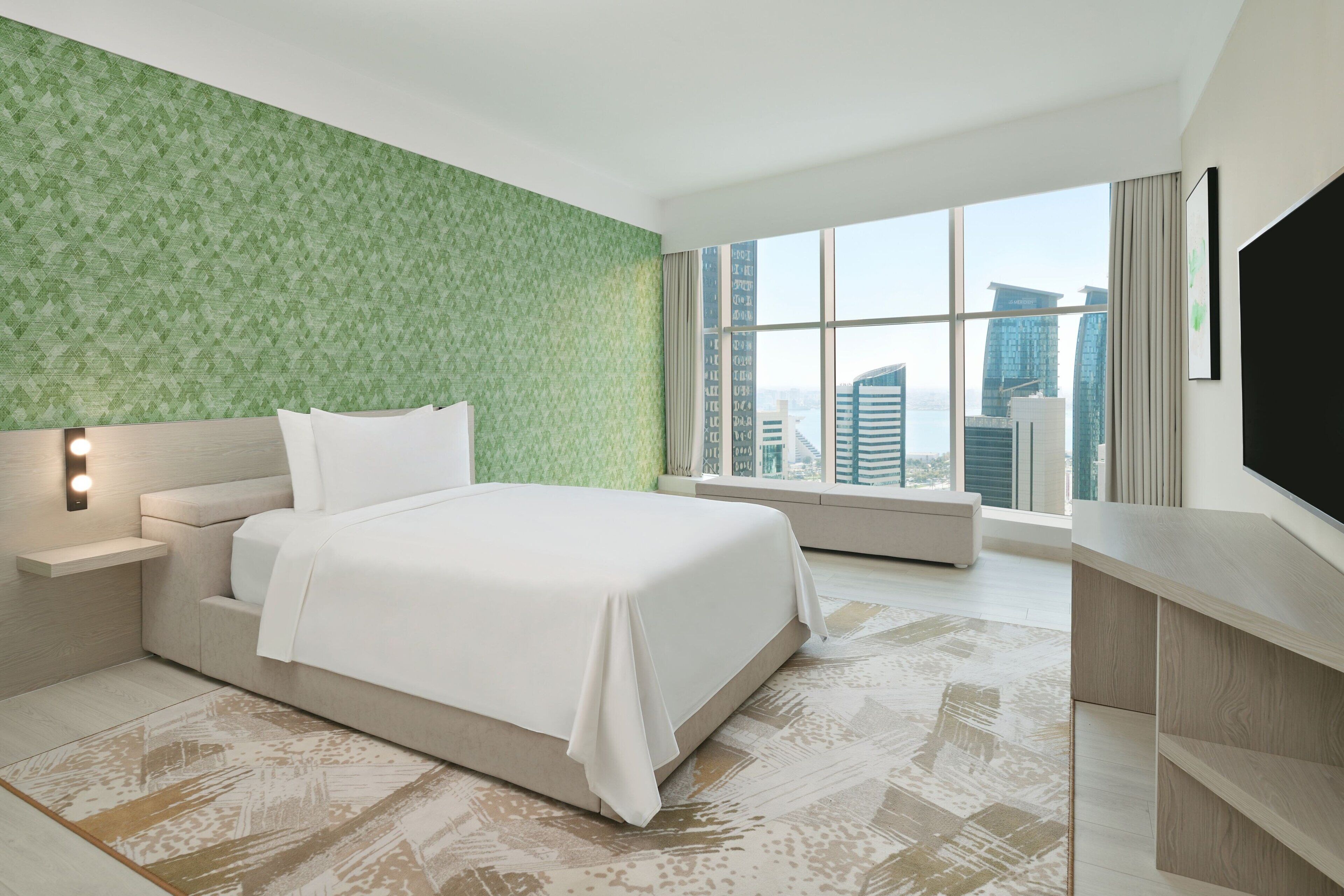 Habitación de hotel moderna con una cama grande, televisión, mesita de noche y vistas a la ciudad desde la ventana.